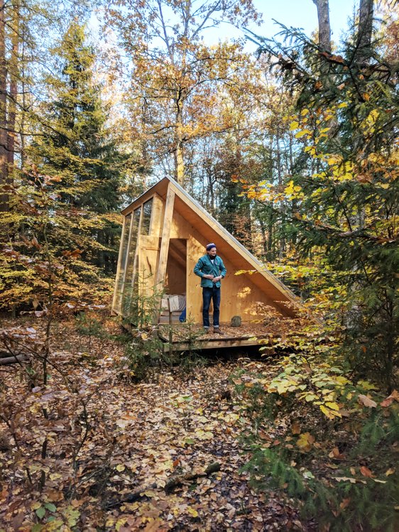 An A-frame cabin in the autumn with a man on the terrace